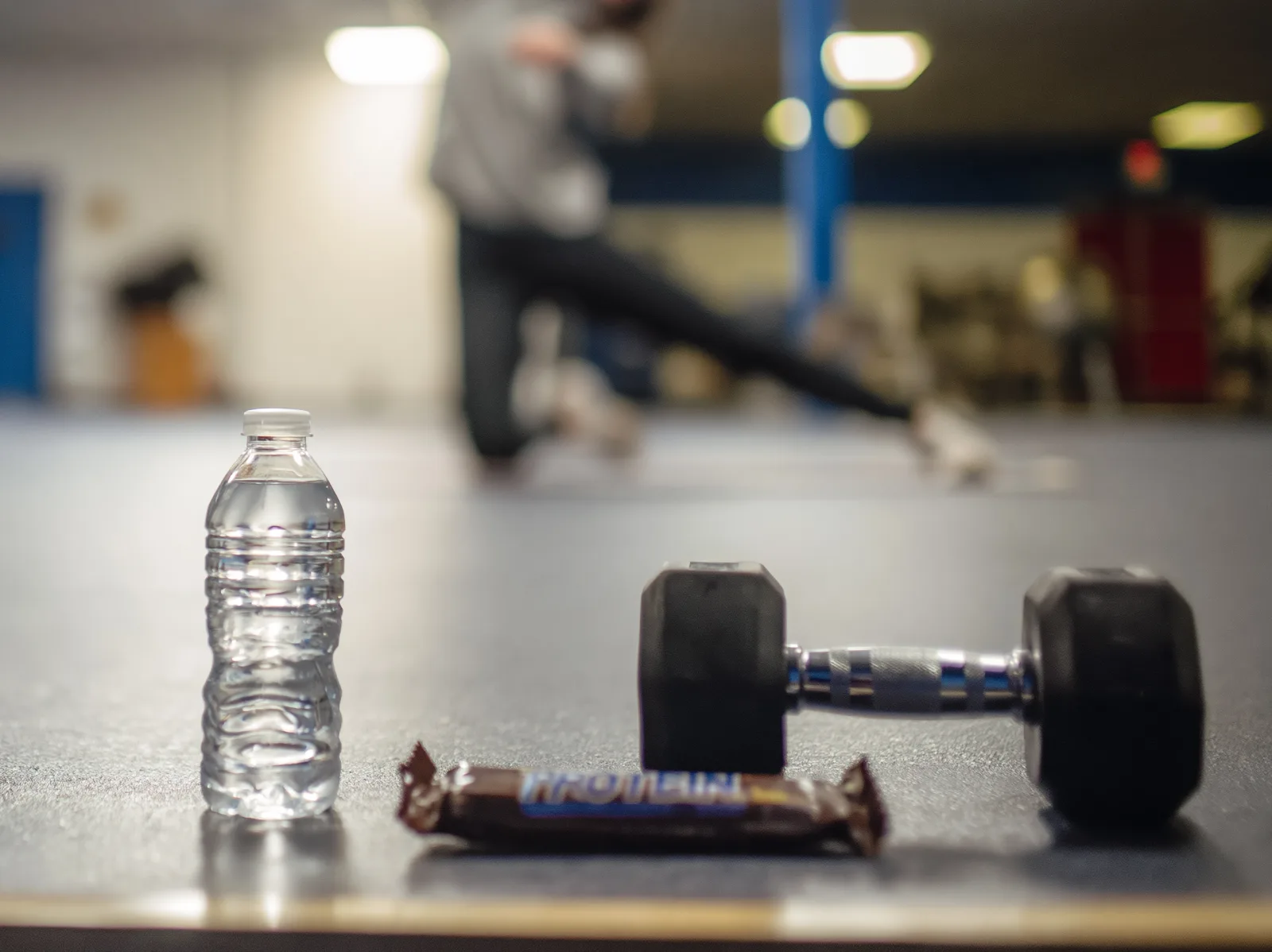 Halter waterfles en proteïnereep op de vloer in de sportschool